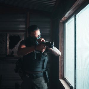 A soldier in a bulletproof vest by the window checks his weapon