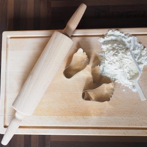 A wooden board with a pile of flour, foot molds and a rolling pin on it