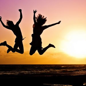 Two girls on the beach are jumping at sunset