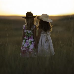 Sisters hold each other and stand in the pasture in the sunset