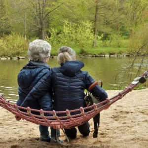 Two women are sitting in a hammock on the river bank