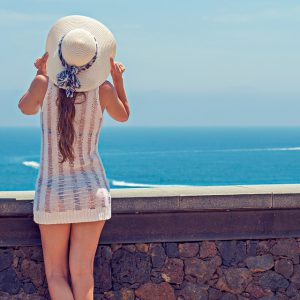 A woman with a hat is looking at the sea